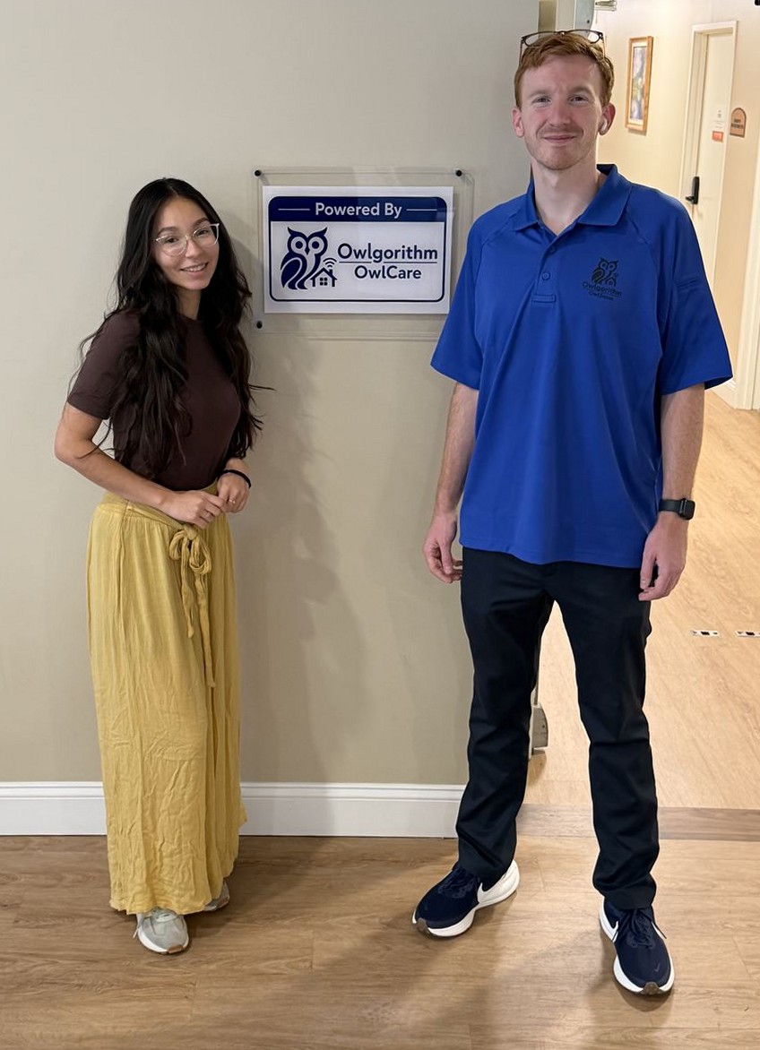Founders Eli and Daniela beside the Powered By Owlgorithm sign in a facility hallway